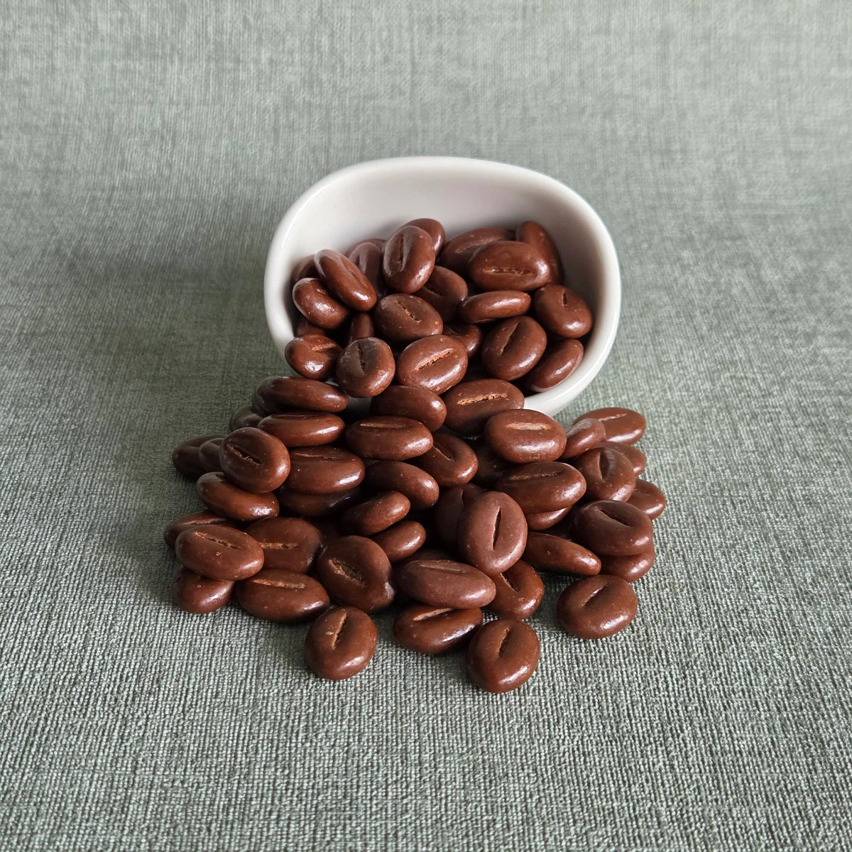 Melkchocoladebonen uit een wit bakje op een grijze ondergrond, Velvet Chocolate Beans