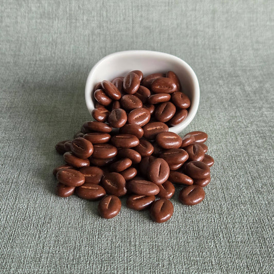 Melkchocoladebonen uit een wit bakje op een grijze ondergrond, Velvet Chocolate Beans