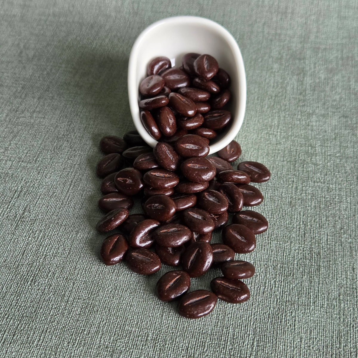 Donkerbruine chocoladebonen uit een wit bakje op een grijze ondergrond, Midnight Chocolate Beans