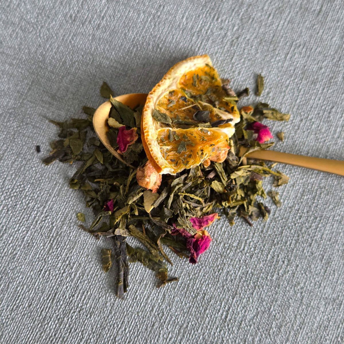 Gouden lepel met groene sencha van Christmas Sencha met gedroogde sinaasappelschijf en rozenknoppen
