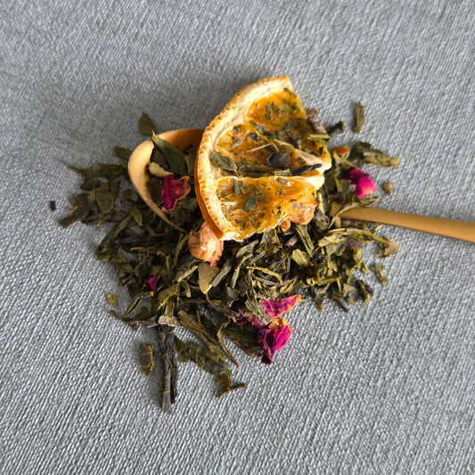 Gouden lepel met groene sencha van Christmas Sencha met gedroogde sinaasappelschijf en rozenknoppen
